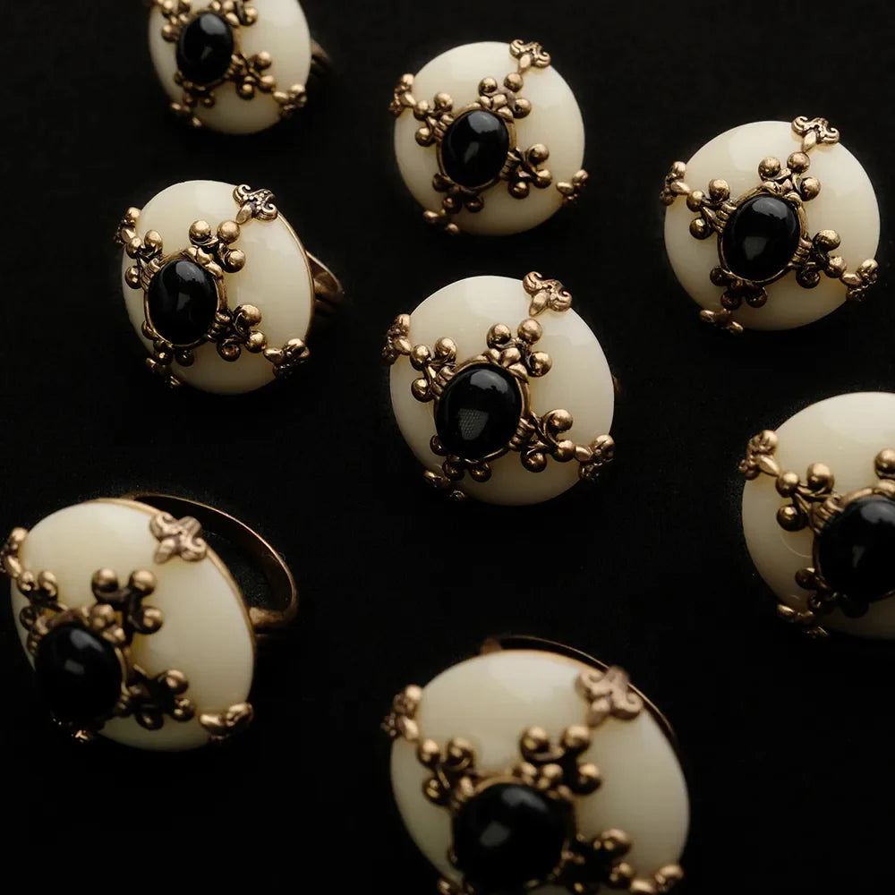 Plusieurs bagues ornées d'une agate noire centrale, sertie sur une monture ovale crème entourée de détails dorés filigranés sur fond noir.