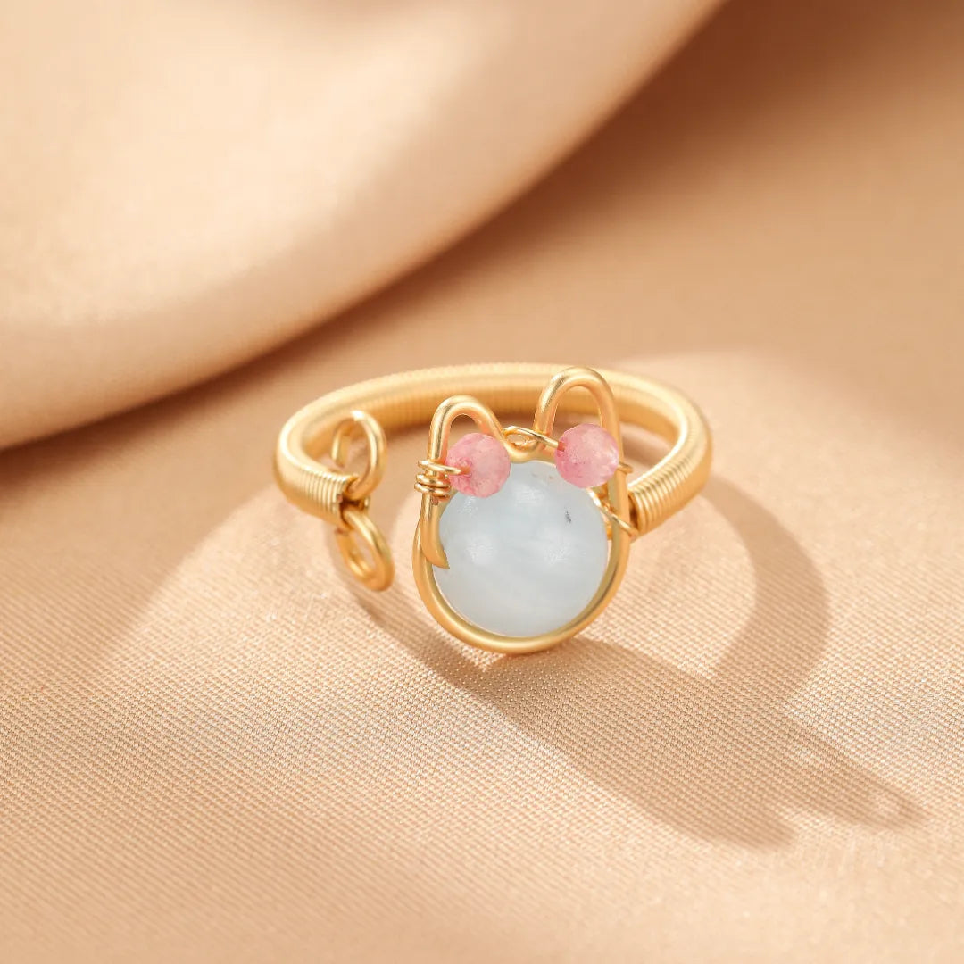 Bague dorée 14K "Chaton Joyeux" ornée d'une pierre naturelle bleu pâle et de deux petites perles roses formant des oreilles.