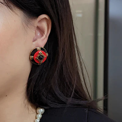 Boucles d'oreilles rondes style vintage, ornées d'une agate noire centrale, d'un contour rouge et de détails dorés, portées par une femme.