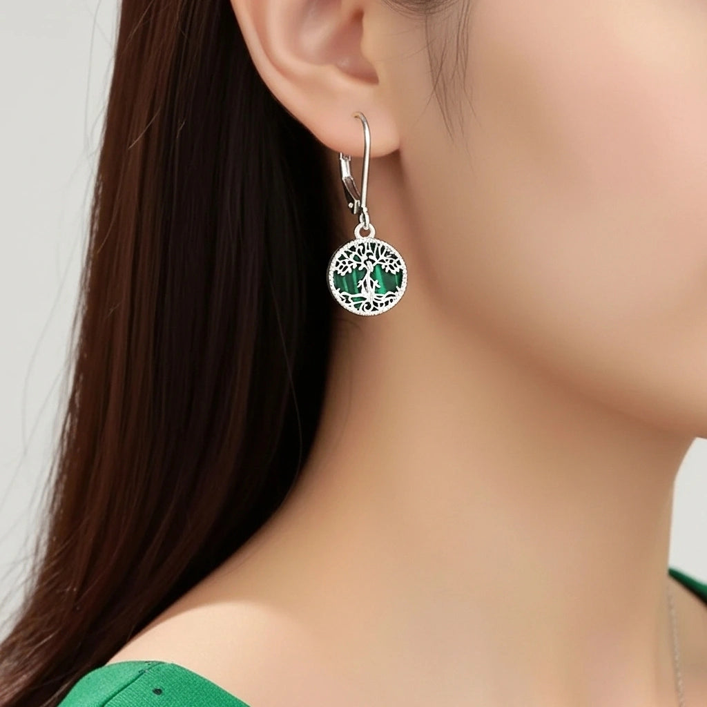 Boucles d'oreilles pendantes en argent ornées d'un motif d'arbre de vie avec une pierre verte incrustée, vues portées sur une oreille.