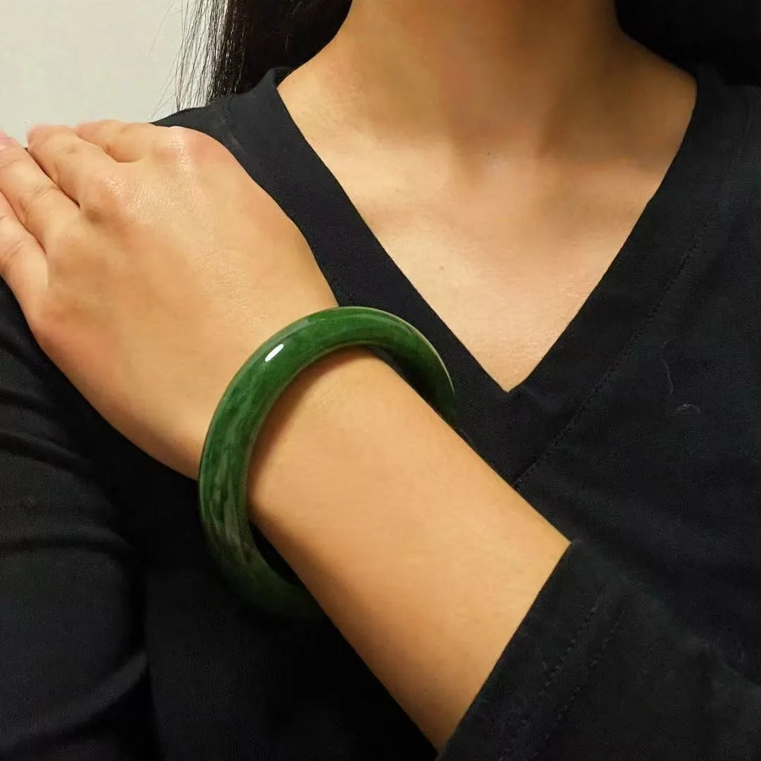 Bracelet jonc en jade "Verdure Éternelle" porté au poignet d'une femme, mettant en valeur sa couleur verte profonde et ses marbrures naturelles.