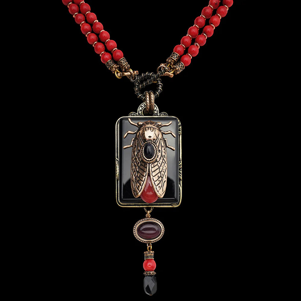 Collier fantaisie avec pendentif en forme de cicadelle en métal bronze, orné d'une agate noire rectangulaire, d'une pierre rouge goutte et d'une pierre ovale bordeaux, monté sur un double rang de perles rouges corail.