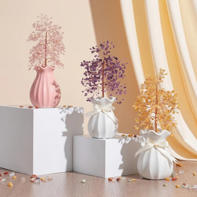 Trois arbres de vie décoratifs en pierres naturelles : rose, violet et jaune, présentés dans des vases blancs et roses sur des podiums.