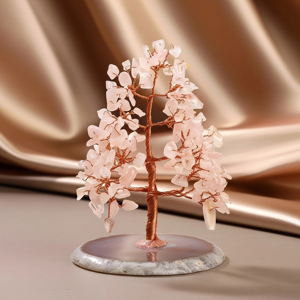 Arbre de vie décoratif en quartz rose avec des branches en fil de cuivre et une base en agate sur un fond satiné brun.