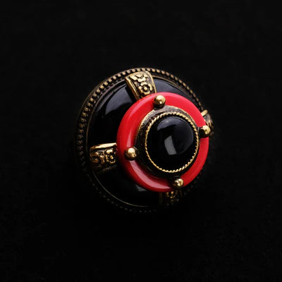 Bague "Merveille d'Antan" avec une pierre centrale noire, entourée d'un anneau rouge et d'une monture dorée sur fond noir