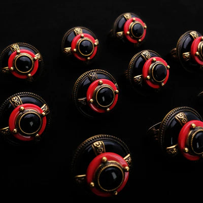 Plusieurs bagues de style vintage avec une pierre centrale noire, un anneau rouge et des détails dorés, présentées sur un fond noir. La bague 'Merveille d'Antan' est ornée d'agate.