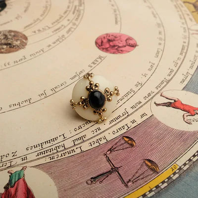 Bague en agate noire et crème avec un design doré orné de motifs de croix, posée sur une ancienne carte astrologique.