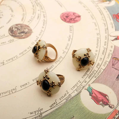 Trois bagues "Pureté Mystique" avec une agate noire centrale et des ornements dorés sur un fond de carte astrologique.