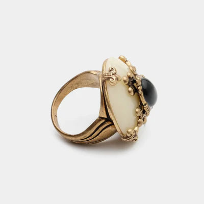 Bague "Pureté Mystique" en argent doré ornée d'une pierre centrale d'agate noire cabochon et d'une monture en résine crème avec des détails dorés complexes.
