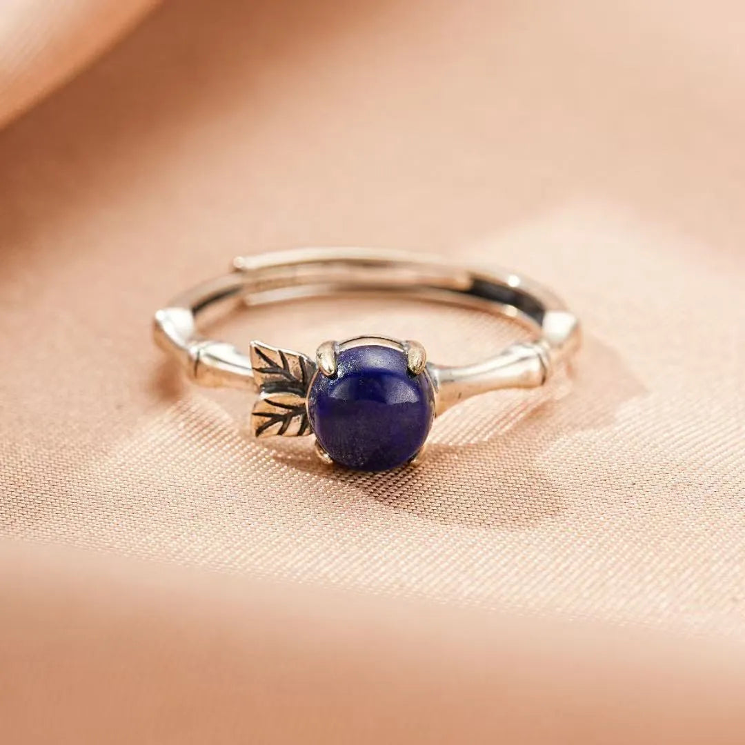 Bague ajustable en argent avec une pierre de lapis-lazuli ronde et bleue sertie sur un anneau torsadé orné d'une petite feuille.