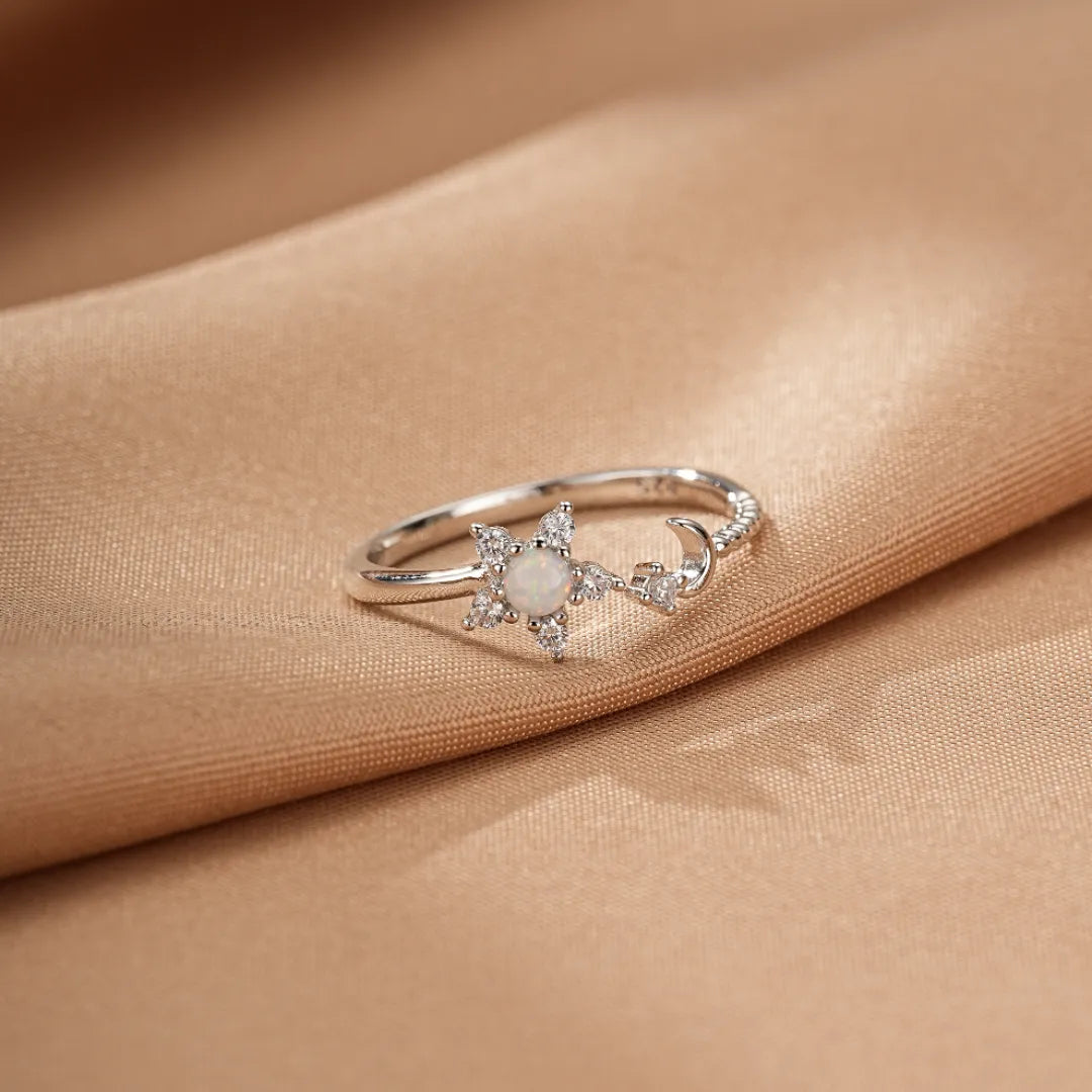 Bague en argent ornée d'une opale centrale en forme d'étoile entourée de petites pierres scintillantes, avec un croissant de lune stylisé à côté.