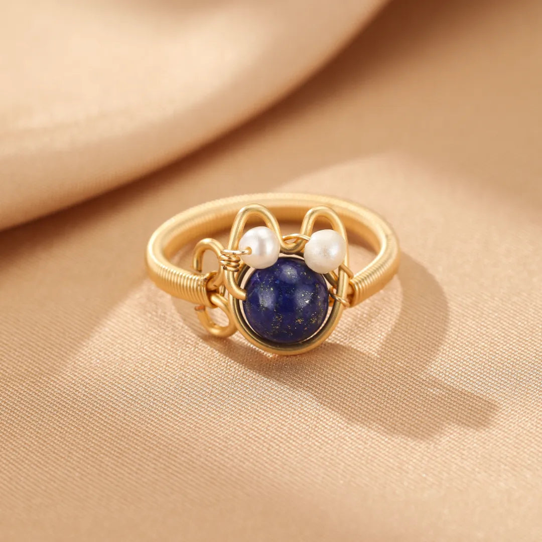 Bague fantaisie dorée or 14K avec une pierre bleue lapis-lazuli et deux petites perles nacrées formant un visage de chaton joyeux.
