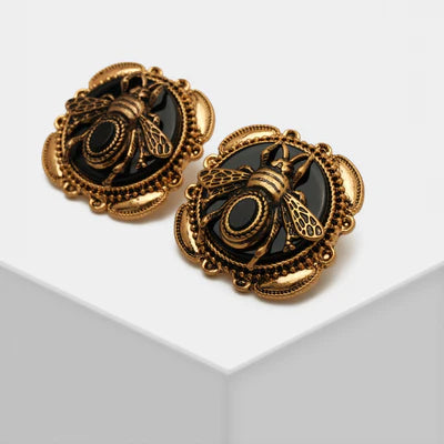 Boucles d'oreilles dorées ornées d'une abeille en relief sur fond noir, style vintage.