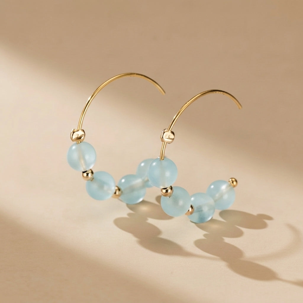 Paire de boucles d'oreilles créoles en or jaune serties de perles d'aigue-marine bleues claires et de petites perles dorées. @main