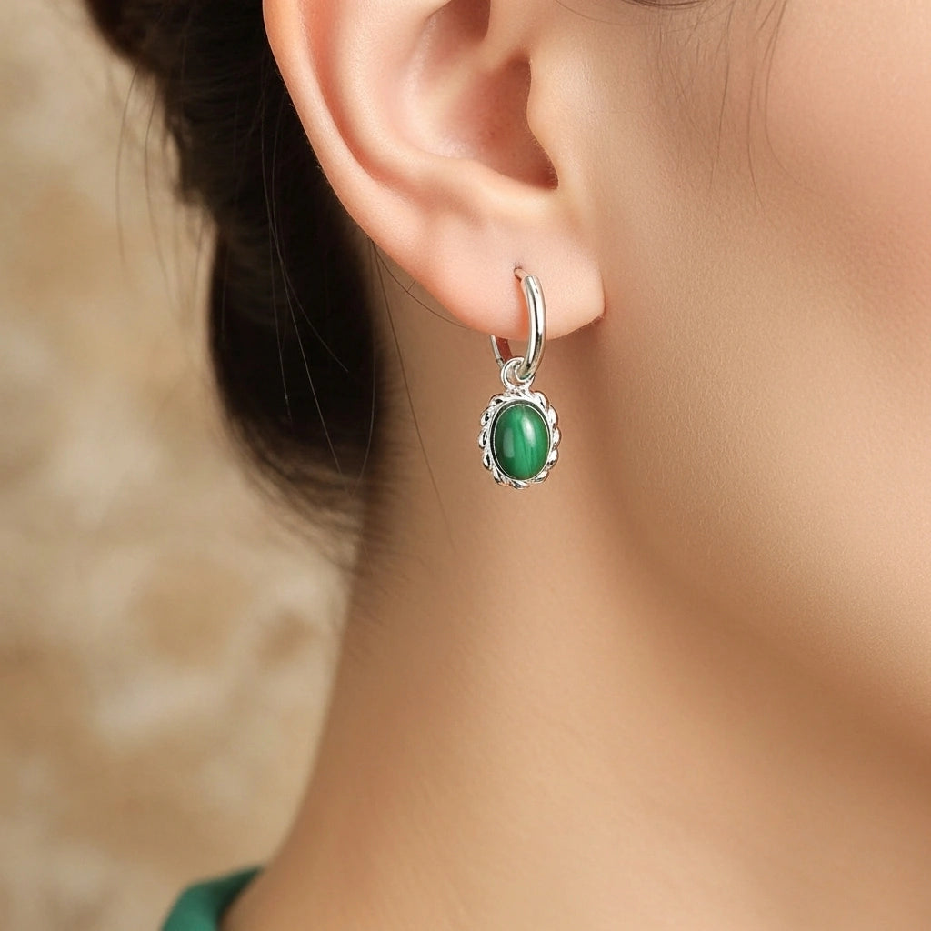 Boucles d'oreilles pendantes en argent ornées d'une pierre de malachite ovale, sertie dans un cadre torsadé, portées par une femme.