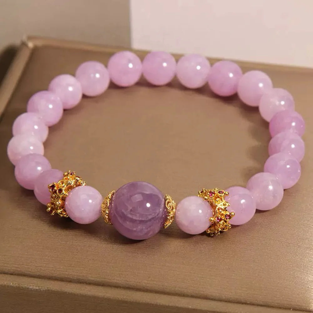 Bracelet élastique fait de perles d'améthyste et de perles roses pâles, rehaussé de deux ornements dorés sertis de petites pierres rouges.