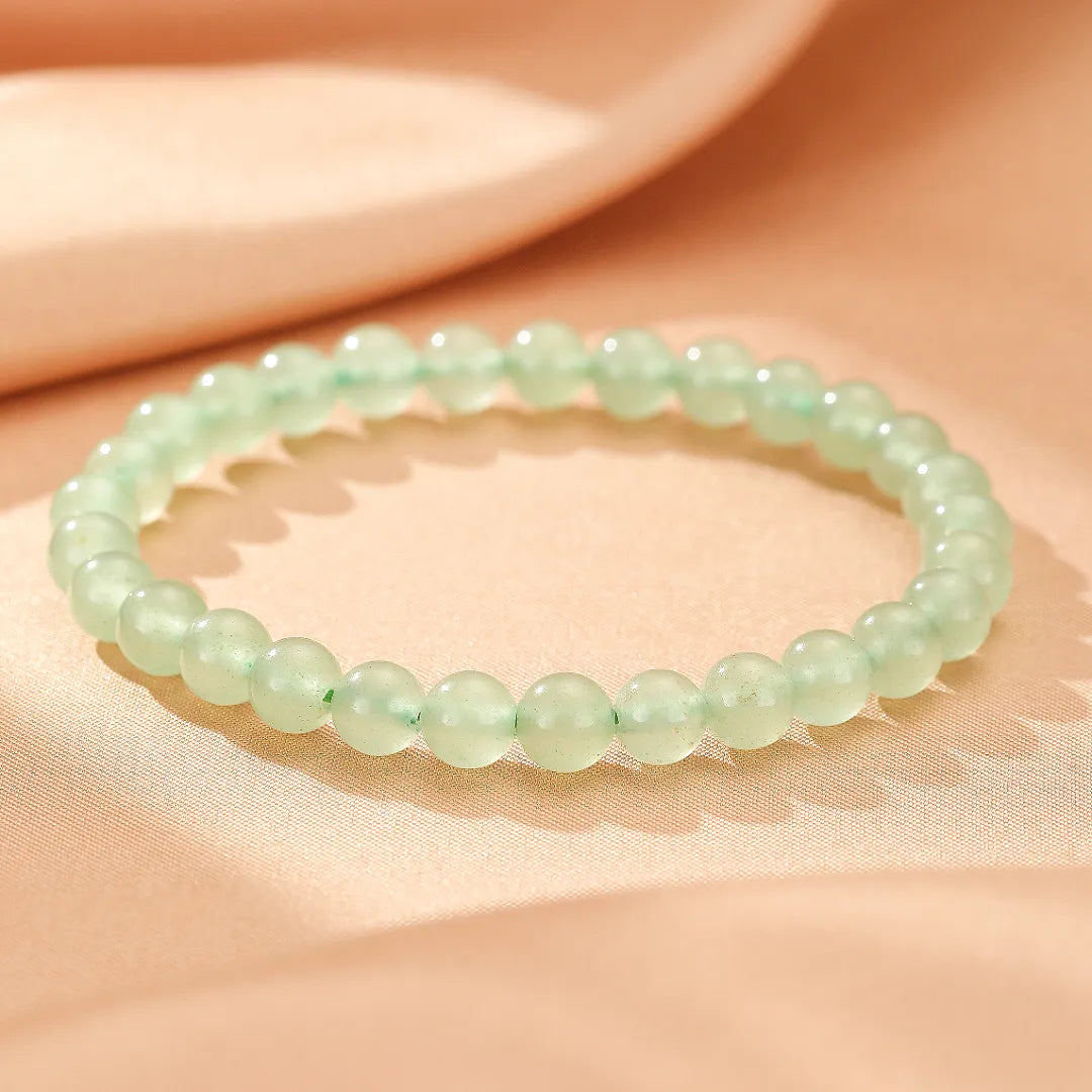 Bracelet fait de perles d'aventurine verte pâle "Énergie Douce" sur un fond de tissu satiné.