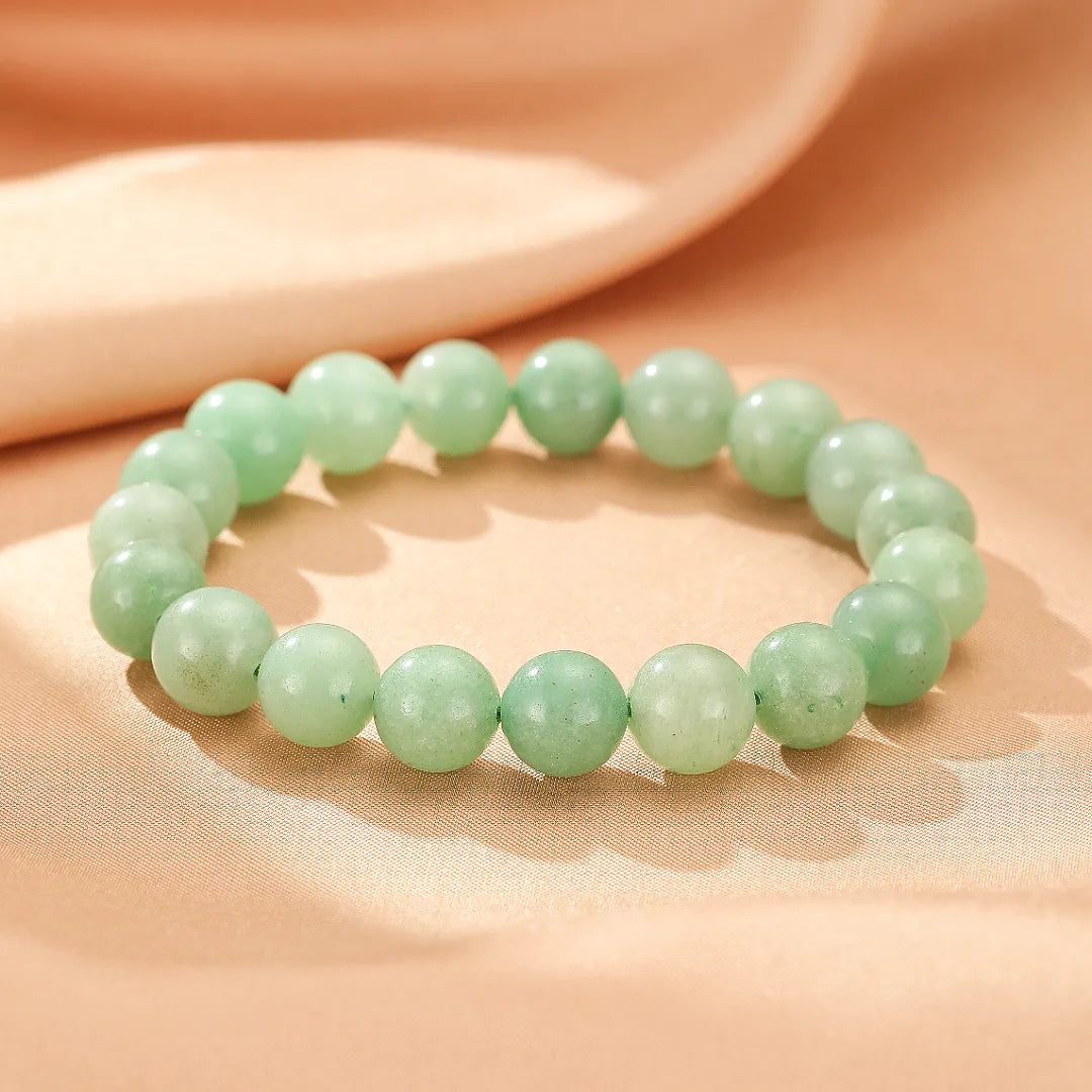 Bracelet en aventurine "Énergie Douce" avec des perles vertes pâles sur un tissu satiné de couleur pêche.