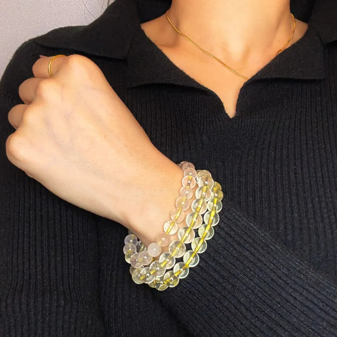 Bracelet Citrine "Lumière Intérieure" porté au poignet d'une femme, composé de perles transparentes et jaunes reliées par un fil élastique doré.