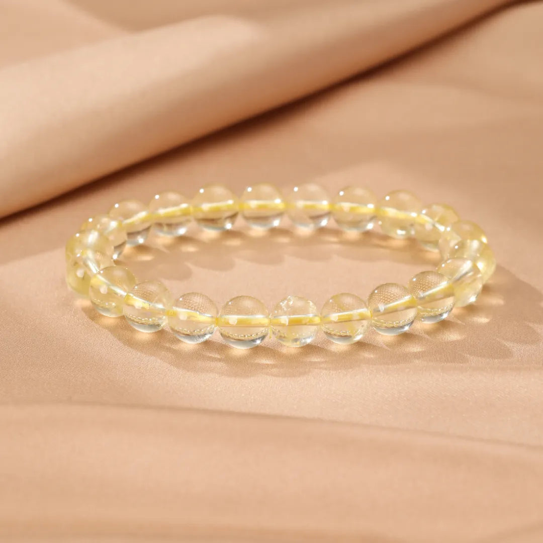 Bracelet fait de perles rondes de citrine lumineuse et transparente, montées sur un fil élastique jaune, posé sur un fond beige doux.