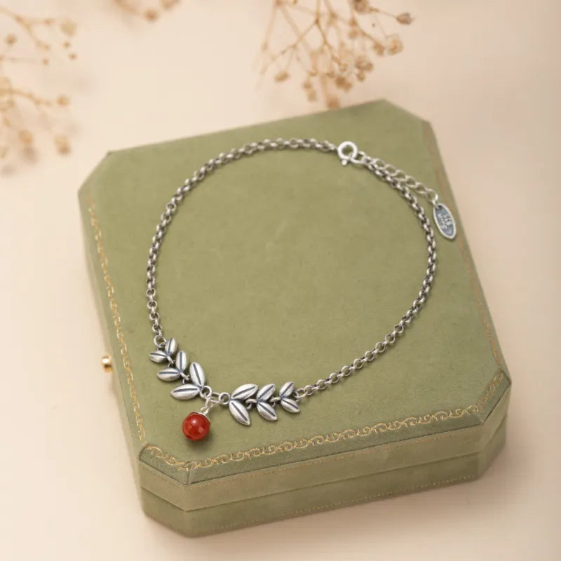 Bracelet de cheville en argent orné de feuilles stylisées et d'une perle d'agate rouge, posé sur une boîte à bijoux verte.