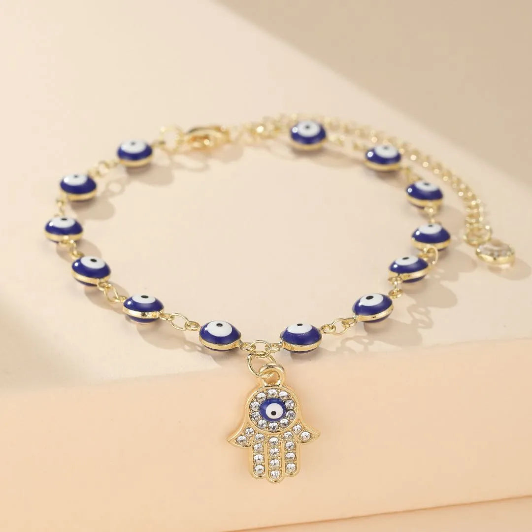 Bracelet de cheville doré orné de plusieurs perles œil bleu et d'une breloque main de Fatma sertie de strass.