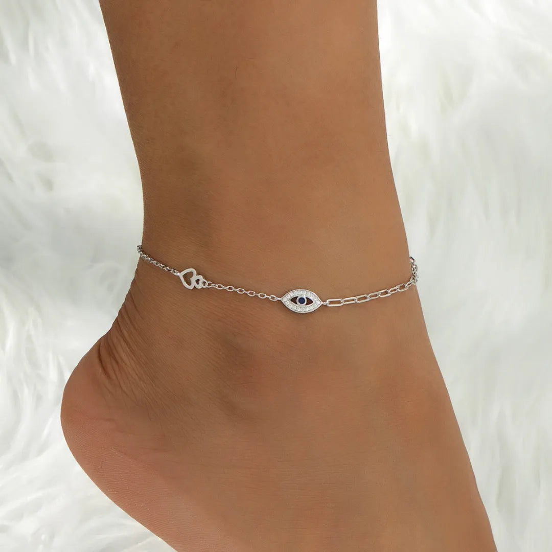 Bracelet de cheville en argent 925 avec un motif œil bleu et un petit cœur ajouré sur une cheville féminine.