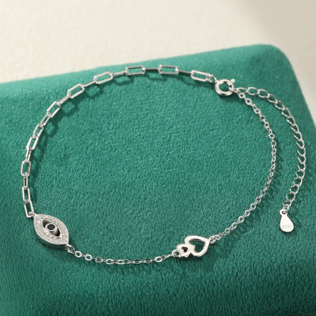 Bracelet de cheville en argent 925 "Protection Élégante" orné d'un œil maléfique serti de zirconiums et d'un motif de deux cœurs entrelacés.
