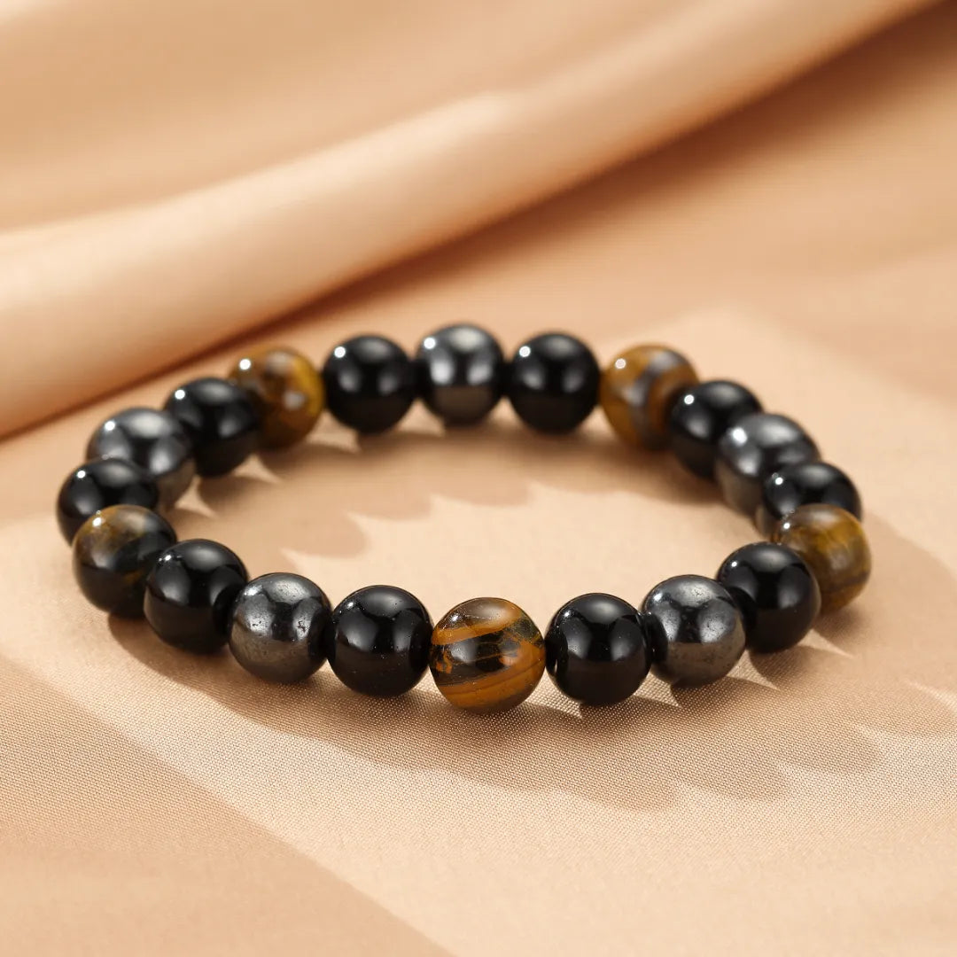 Bracelet "Force Protectrice" en œil de tigre et hématite avec des perles rondes alternées sur un fond beige.