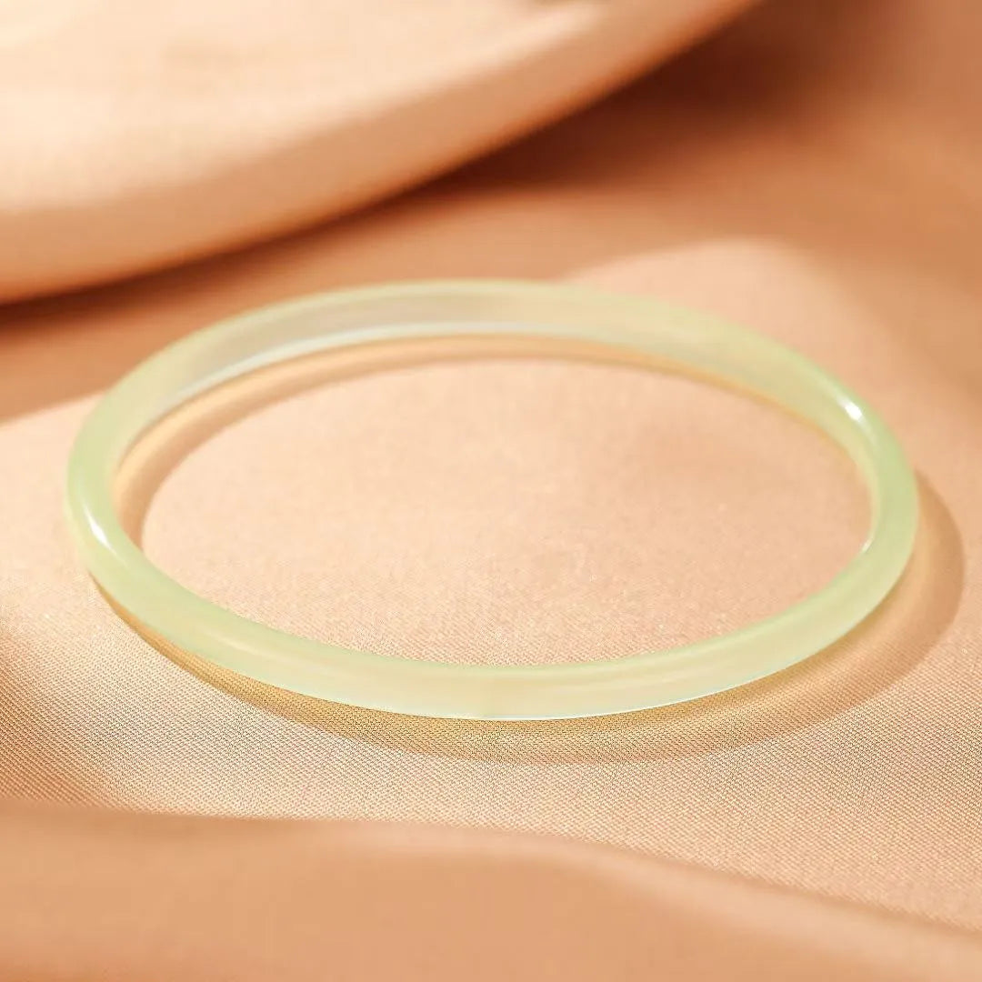 Bracelet jonc en calcédoine vert pâle, au design épuré et translucide, posé sur un tissu satiné beige.
