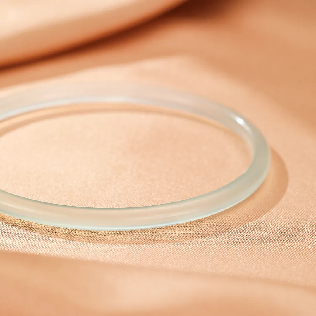 Bracelet jonc fin en calcédoine translucide aux reflets aquatiques, posé sur un tissu satiné couleur pêche.