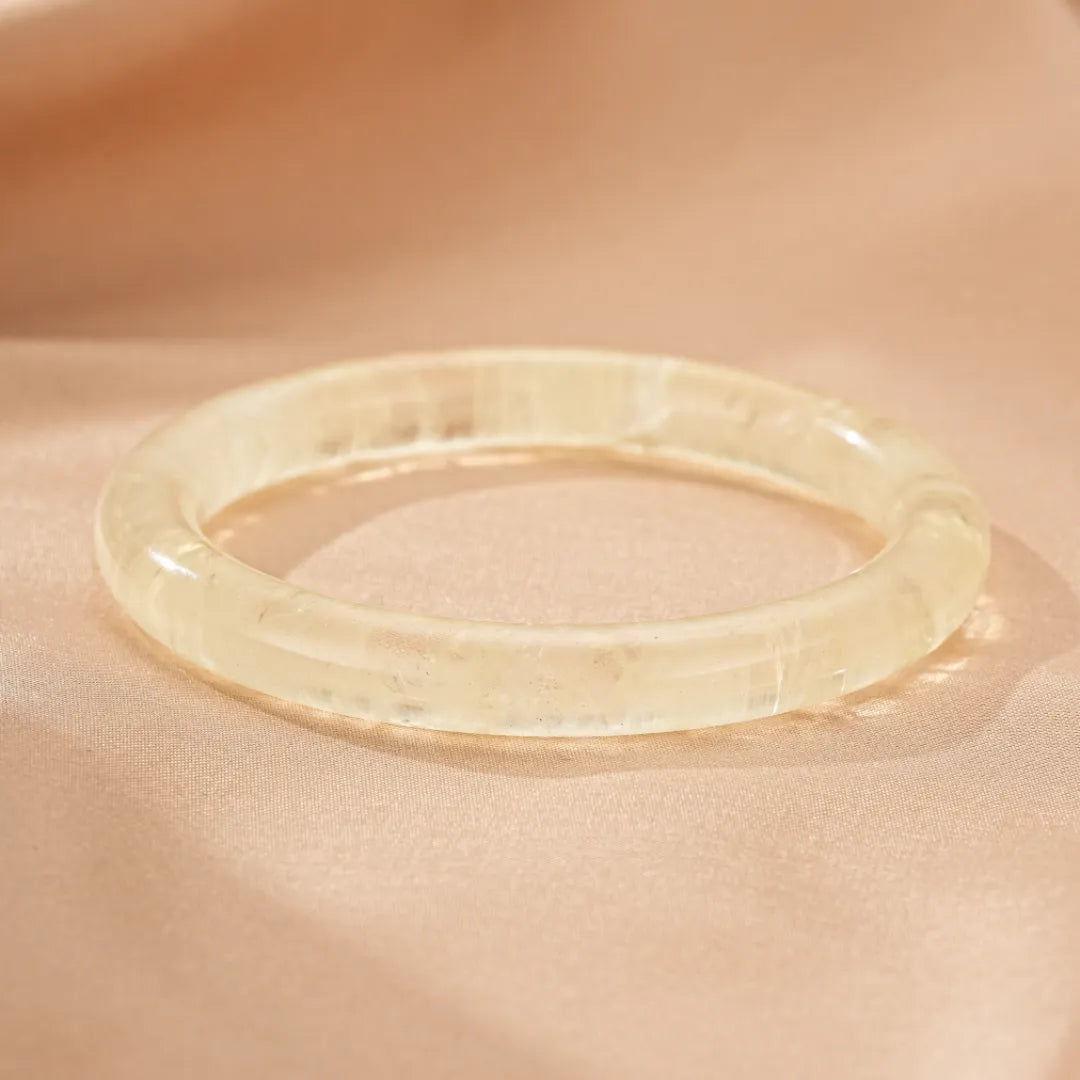 Bracelet jonc transparent en citrine naturelle, le bijou "Reflets de Confiance" posé sur un tissu satiné couleur pêche.