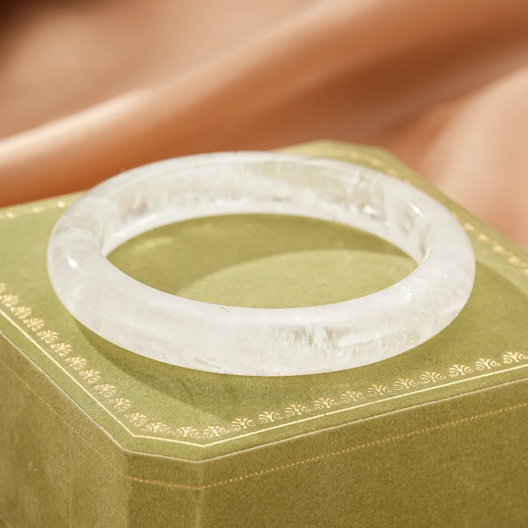 Bracelet jonc en cristal de roche naturel, bijou transparent et lumineux, posé sur une boîte cadeau verte.