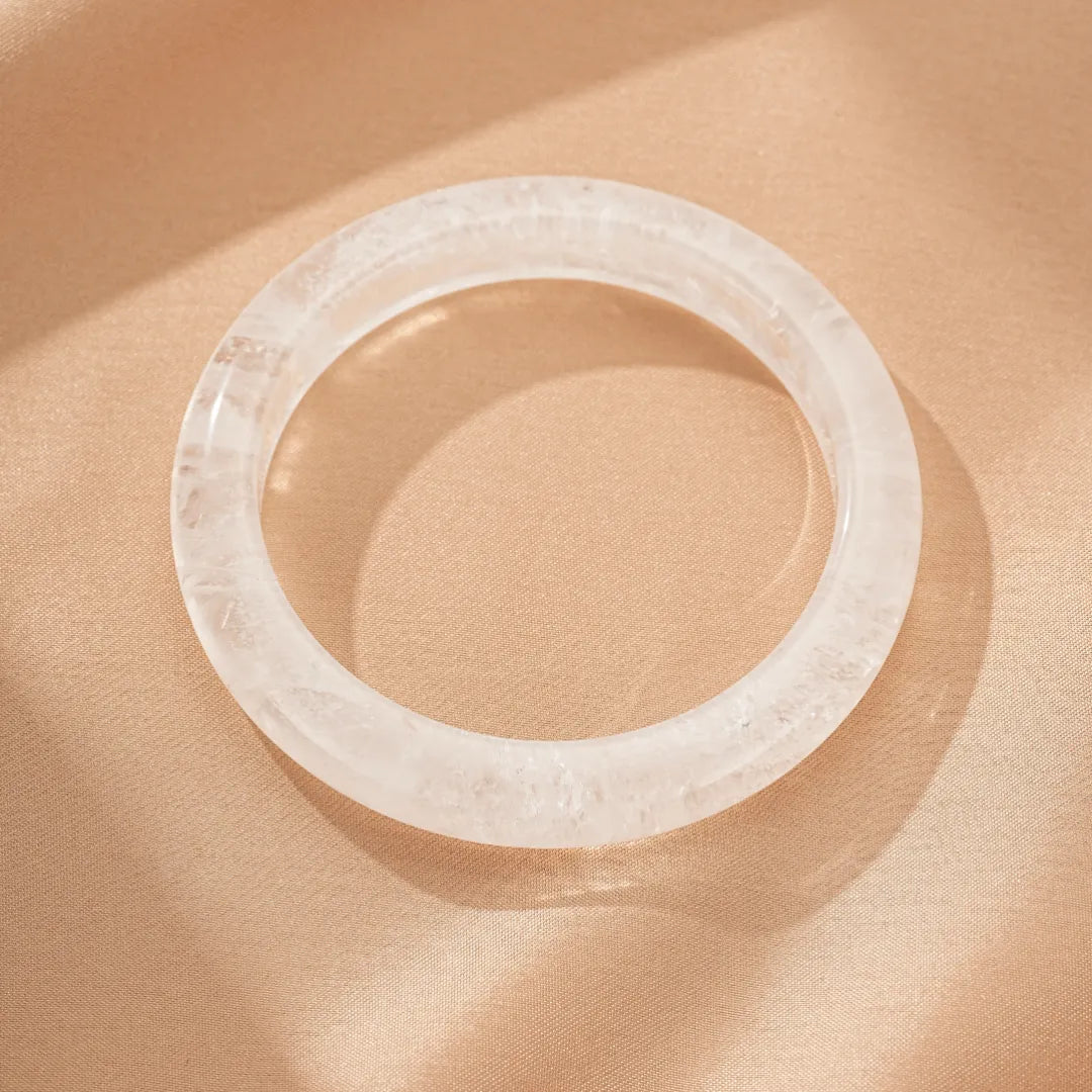 Bracelet jonc en cristal de roche naturel, bijou transparent et lumineux sur fond satiné.
