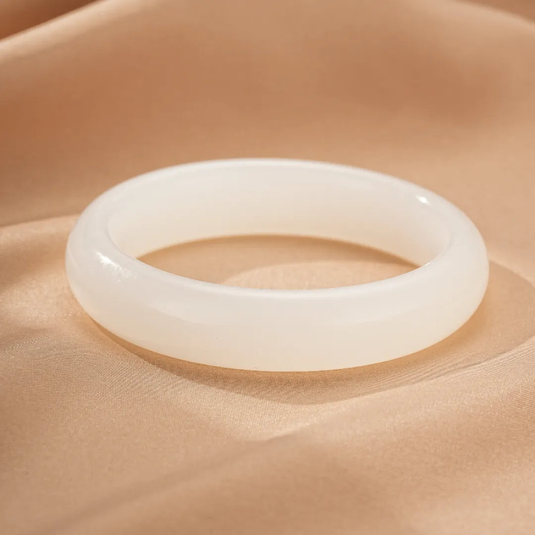 Bracelet jonc en jade blanc, symbole de paix intérieure, sur fond satiné beige.