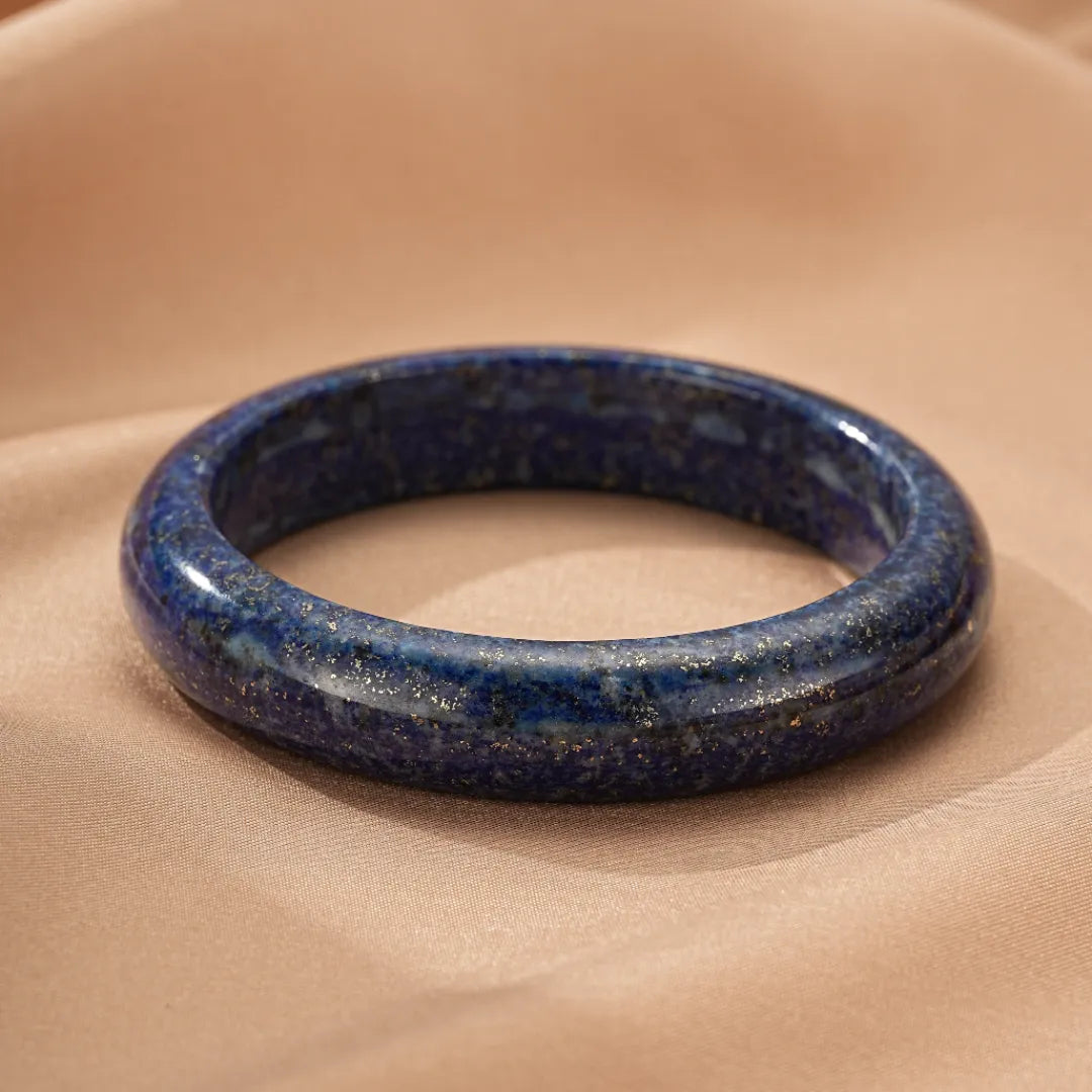 Bracelet jonc en lapis lazuli, avec des inclusions dorées, sur un fond beige satiné.