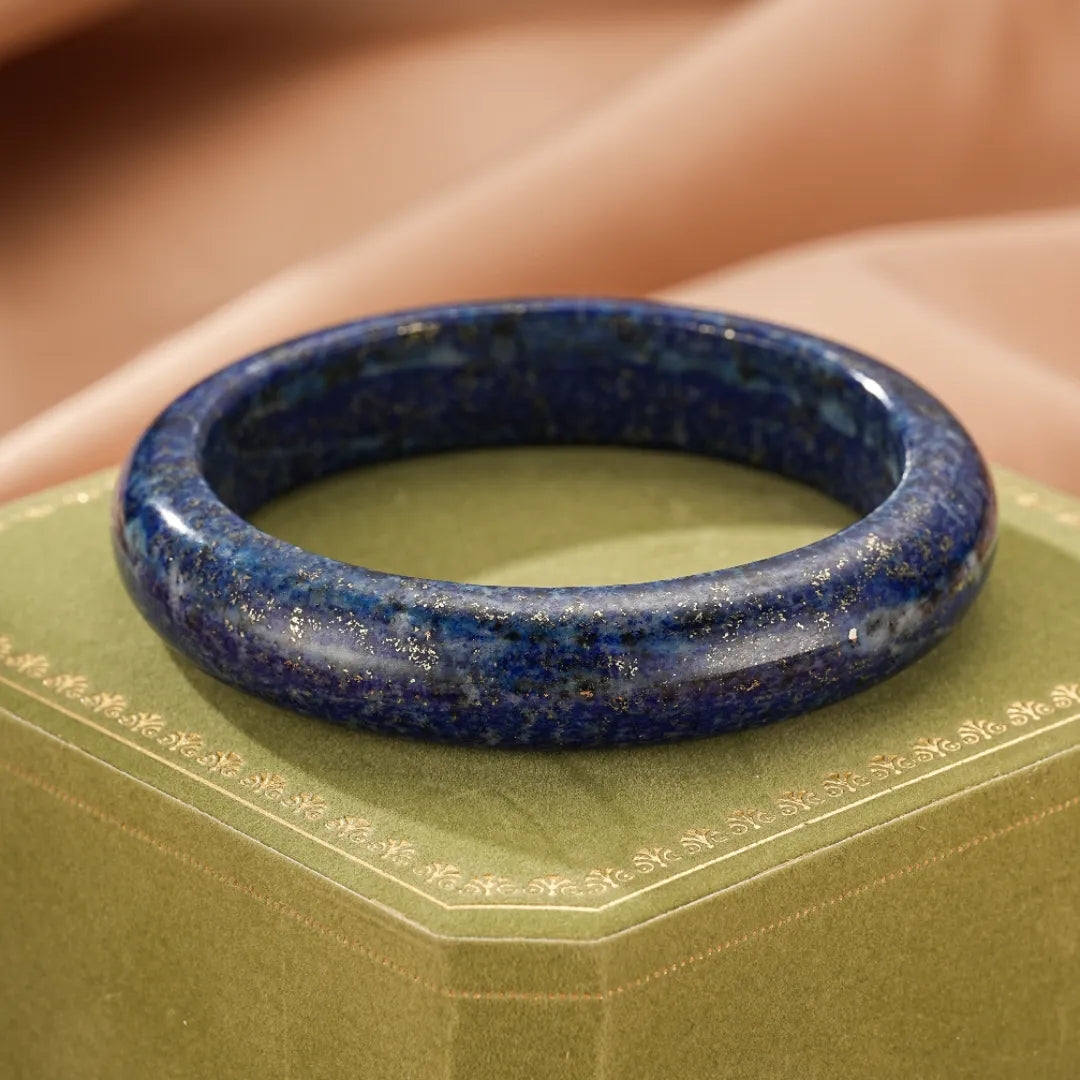 Bracelet jonc en lapis lazuli naturel, orné d'inclusions dorées, posé sur un écrin vert sapin.