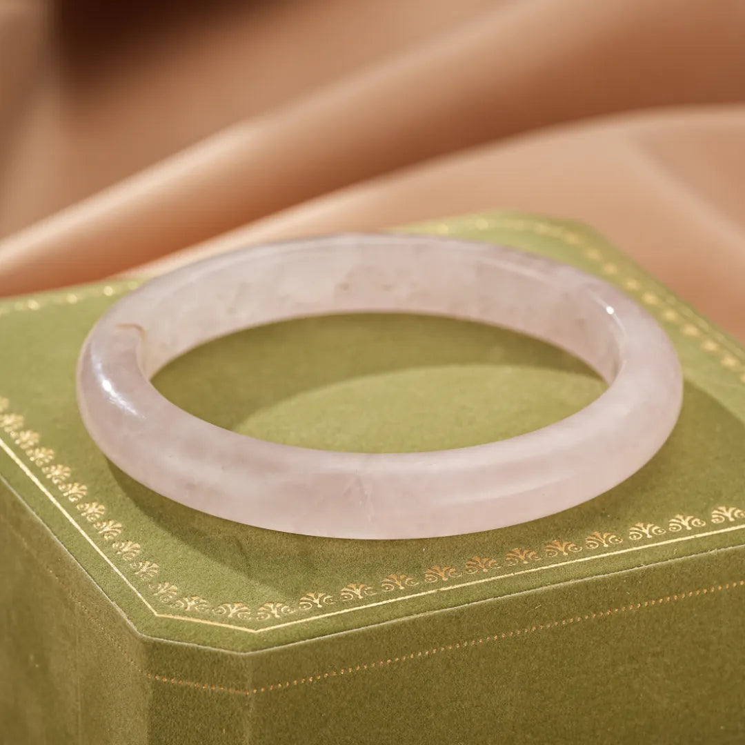 Bracelet jonc en quartz rose, symbolisant l'amour inconditionnel, posé sur une boîte verte ornée de motifs dorés.