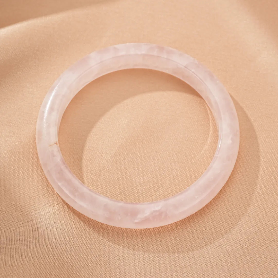 Bracelet jonc en quartz rose naturel, bijou symbolisant l'amour inconditionnel, sur fond satiné.