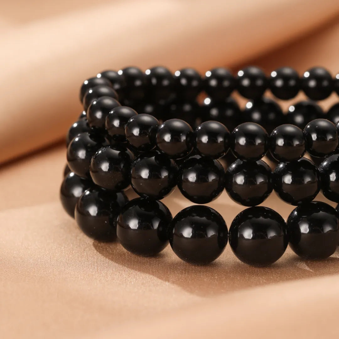 Bracelet triple rangs en perles d'obsidienne naturelle polies sur un fond satiné beige.