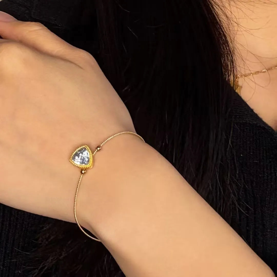 Bracelet fin en argent doré or avec une topaze bleue en forme de triangle, modèle "Harmonie Céleste" porté au poignet.