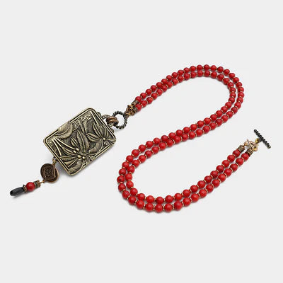 Collier double rang en perles d'agate rouge vif avec un pendentif rectangulaire en métal bronze gravé de motifs floraux.
