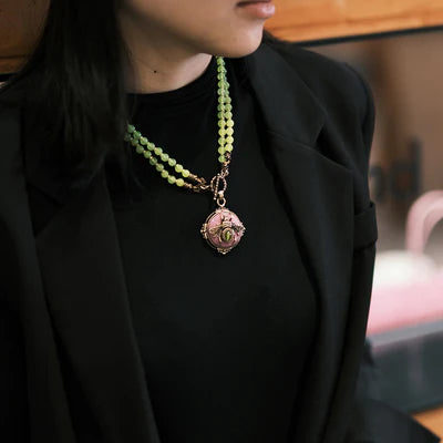 Collier en agate jaune avec un pendentif rond rose orné d'une abeille dorée et verte porté par une femme portant une veste noire