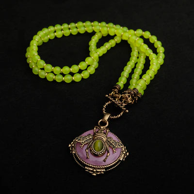 Collier ras du cou à trois rangs de perles rondes vert pomme, orné d'un pendentif carré en agate rose orné d'une abeille dorée avec un cabochon vert au centre et des détails filigranés.