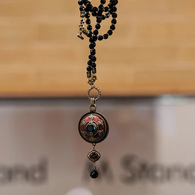 Collier "Merveille d'Antan" en agate avec pendentif rond émaillé rouge et pierre bleue centrale, perles noires facetées et breloque.