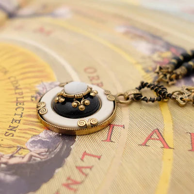 Gros plan sur le pendentif du collier "Pureté Mystique" orné d'une agate noire, d'une pierre blanche et de détails dorés, sur un fond texturé.
