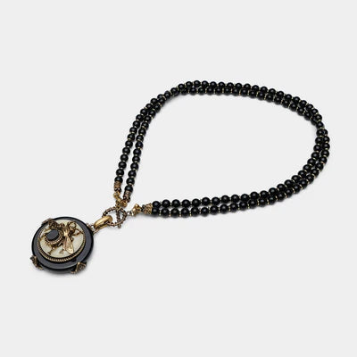 Collier double rangs en agate noire avec pendentif rond orné d'une abeille dorée et d'une pierre sombre.