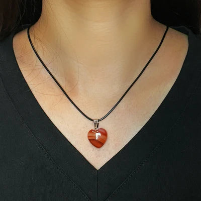Collier "Cœur Confiant" avec un pendentif en forme de cœur d'agate rouge, porté par une femme sur un fond noir.