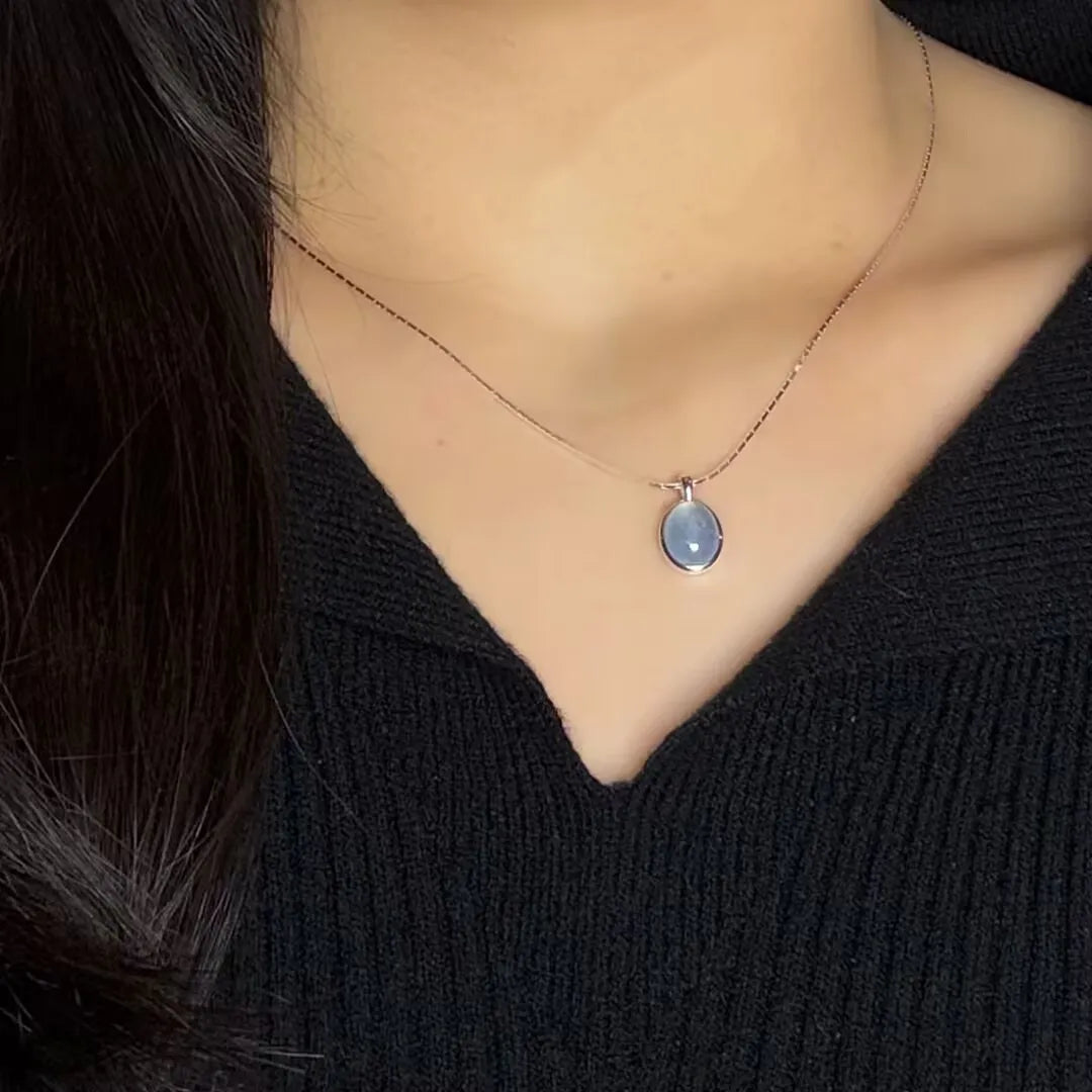 Collier en argent 925 avec un pendentif ovale en aigue-marine bleu clair, porté par une femme portant un pull noir.