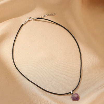 Collier avec pendentif en forme de cœur en améthyste violette sur un cordon noir, avec fermoir argenté.